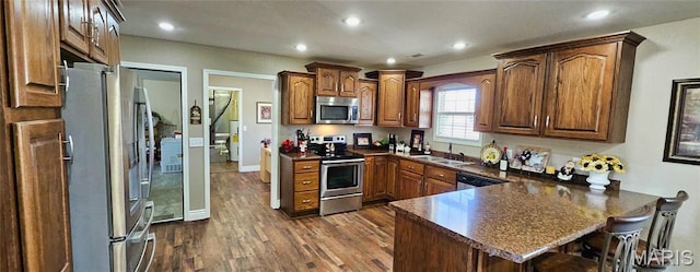 kitchen with stainless steel appliances, a peninsula, dark countertops, dark wood-style floors, and a kitchen breakfast bar