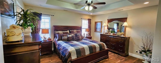 bedroom featuring a tray ceiling, multiple windows, wood finished floors, baseboards, and recessed lighting