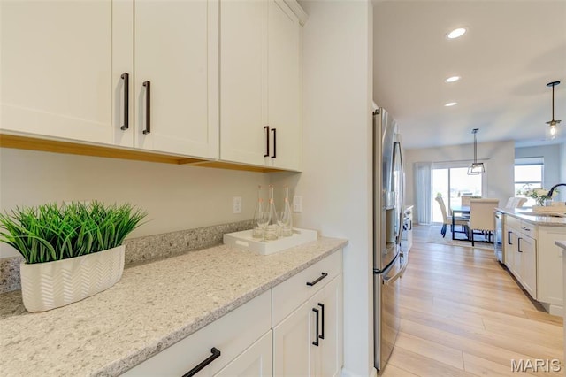 kitchen with a sink, recessed lighting, light wood finished floors, white cabinets, and light stone counters
