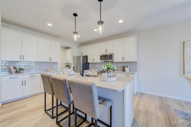 kitchen with stainless steel appliances, a sink, light wood-style floors, decorative backsplash, and a breakfast bar