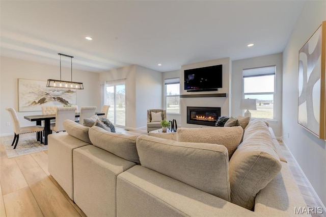 living area featuring light wood-style floors, plenty of natural light, a glass covered fireplace, baseboards, and recessed lighting