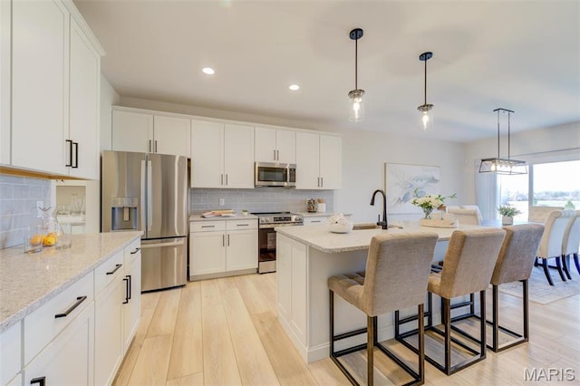 kitchen with stainless steel appliances, a sink, light wood-style flooring, a kitchen breakfast bar, and recessed lighting
