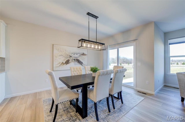 dining area featuring light wood-type flooring, baseboards, and a chandelier
