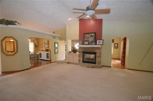 living room with carpet flooring, high vaulted ceiling, baseboards, a stone fireplace, and a ceiling fan