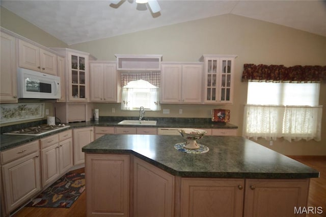 kitchen with white microwave, vaulted ceiling, stainless steel gas stovetop, a sink, and dark countertops