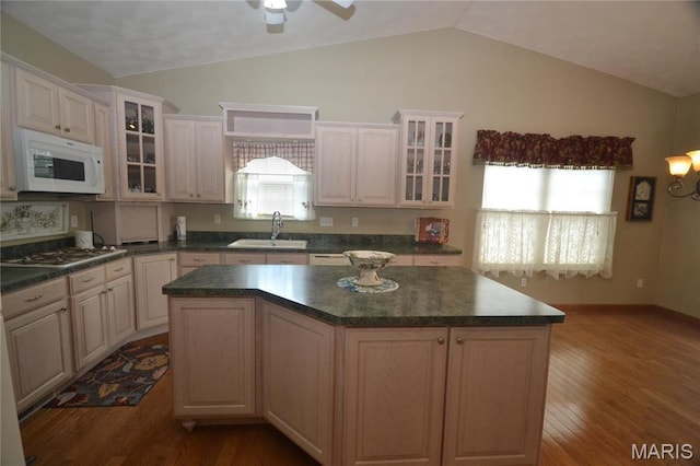 kitchen with white microwave, a sink, lofted ceiling, stainless steel gas stovetop, and dark countertops