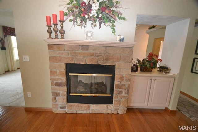 detailed view of a stone fireplace, wood finished floors, and baseboards
