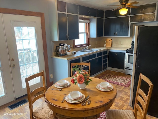 kitchen featuring stainless steel appliances, a sink, light countertops, a ceiling fan, and dark cabinets