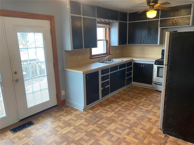 kitchen featuring freestanding refrigerator, a sink, light countertops, stainless steel range with gas cooktop, and ceiling fan