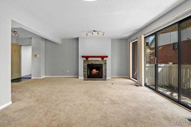 unfurnished living room featuring carpet flooring, baseboards, a fireplace with flush hearth, and a textured ceiling