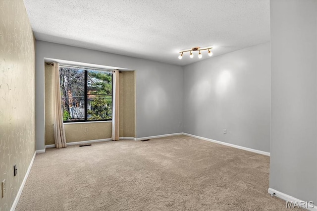 empty room with carpet floors, a textured ceiling, and baseboards