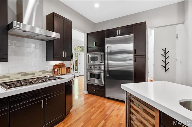 1 W Walinca, Saint Louis, MO 63105 - kitchen featuring built in appliances, wall chimney range hood, light countertops, light wood-style flooring, and wine cooler