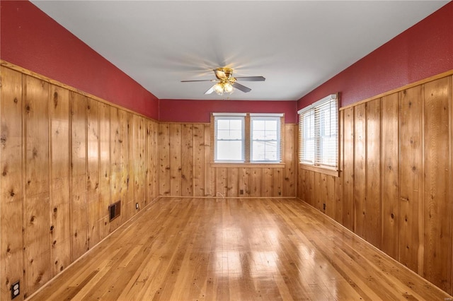 unfurnished room with ceiling fan, wood-type flooring, and wooden walls