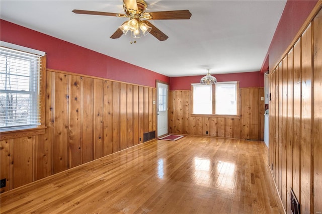 spare room with hardwood / wood-style floors, wood walls, a ceiling fan, and wainscoting
