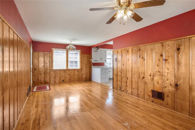 unfurnished living room with wood finished floors, wood walls, washer / clothes dryer, a ceiling fan, and a chandelier