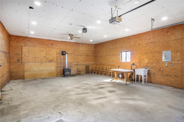 garage with a garage door opener, electric panel, a sink, a wood stove, and ceiling fan