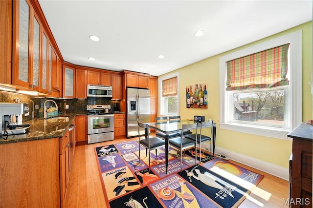 4386 Westminster Pl, Saint Louis, MO 63108 - kitchen with appliances with stainless steel finishes, light wood-type flooring, brown cabinets, decorative backsplash, and glass insert cabinets