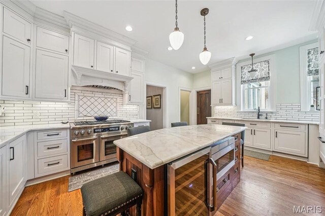 4386 Westminster Pl, Saint Louis, MO 63108 - kitchen with double oven range, wine cooler, backsplash, light wood-type flooring, and recessed lighting