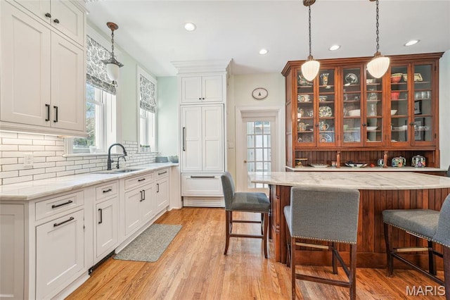 4386 Westminster Pl, Saint Louis, MO 63108 - kitchen with glass insert cabinets, tasteful backsplash, light wood-type flooring, a kitchen breakfast bar, and pendant lighting