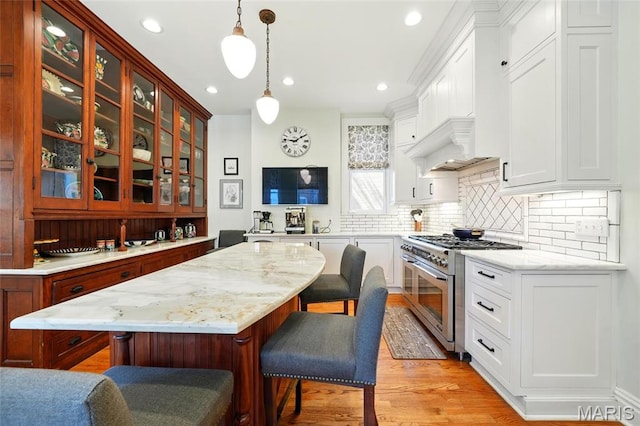 4386 Westminster Pl, Saint Louis, MO 63108 - kitchen with stainless steel stove, glass insert cabinets, a kitchen bar, light wood-style floors, and backsplash