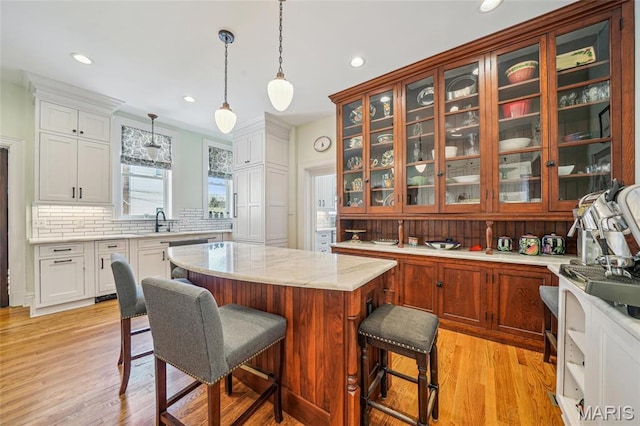 4386 Westminster Pl, Saint Louis, MO 63108 - kitchen with backsplash, a kitchen island, a breakfast bar area, glass insert cabinets, and light wood-type flooring