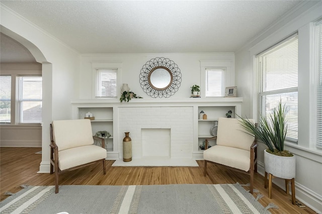 3433 Pine Grove Ave, Saint Louis, MO 63121 - living area with arched walkways, crown molding, wood finished floors, a textured ceiling, and a brick fireplace