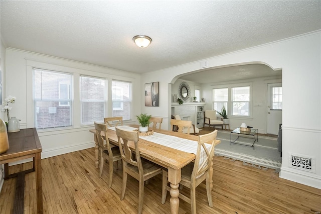 3433 Pine Grove Ave, Saint Louis, MO 63121 - dining space with arched walkways, a textured ceiling, light wood-type flooring, a fireplace, and crown molding