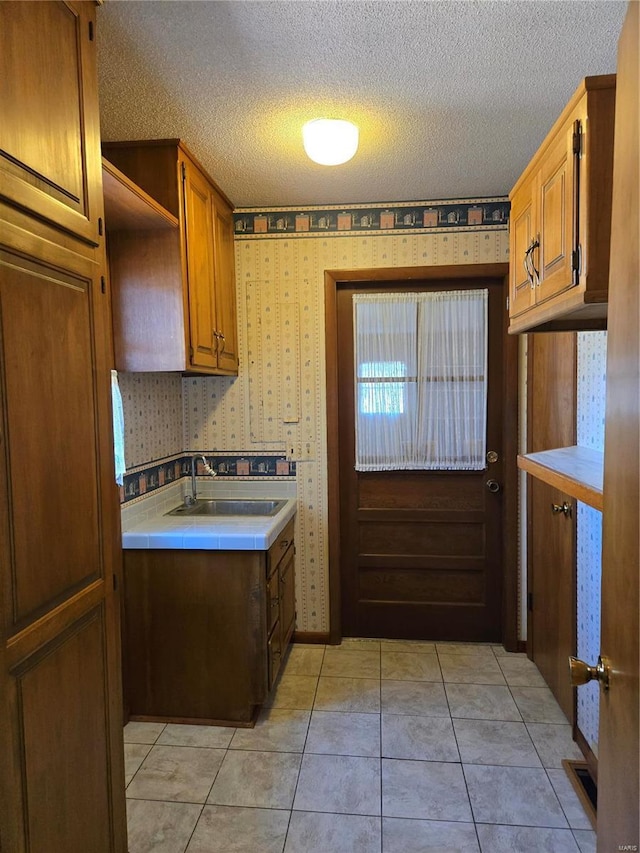 400 Smith Rd, Lebanon, MO 65536 - kitchen featuring a sink, wallpapered walls, a textured ceiling, brown cabinets, and light tile patterned flooring