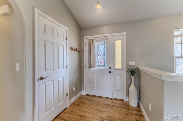 foyer entrance featuring light wood-style flooring, baseboards, and arched walkways