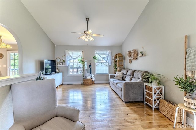living area with lofted ceiling, a ceiling fan, light wood-style floors, arched walkways, and baseboards