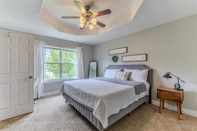 bedroom with a tray ceiling, baseboards, and light carpet