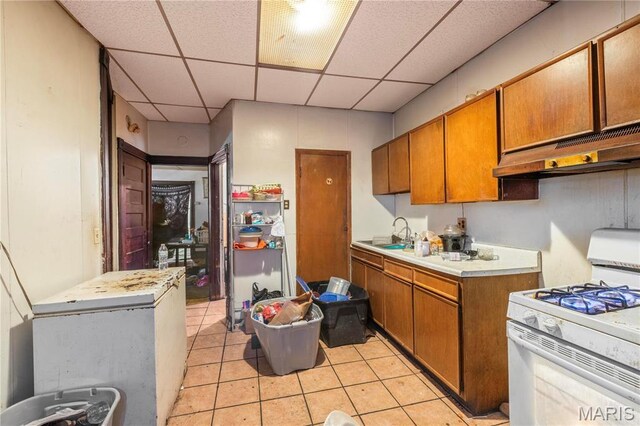 3737 Cottage Ave, Saint Louis, MO 63113 - kitchen featuring white range with gas cooktop, under cabinet range hood, brown cabinets, a drop ceiling, and light tile patterned floors