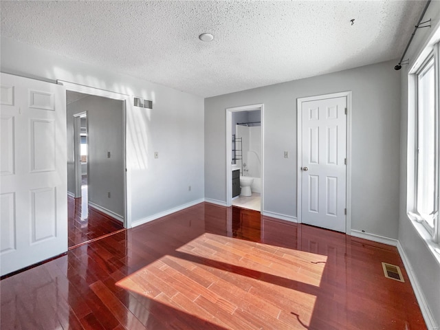 unfurnished bedroom with a textured ceiling, wood finished floors, baseboards, and ensuite bath