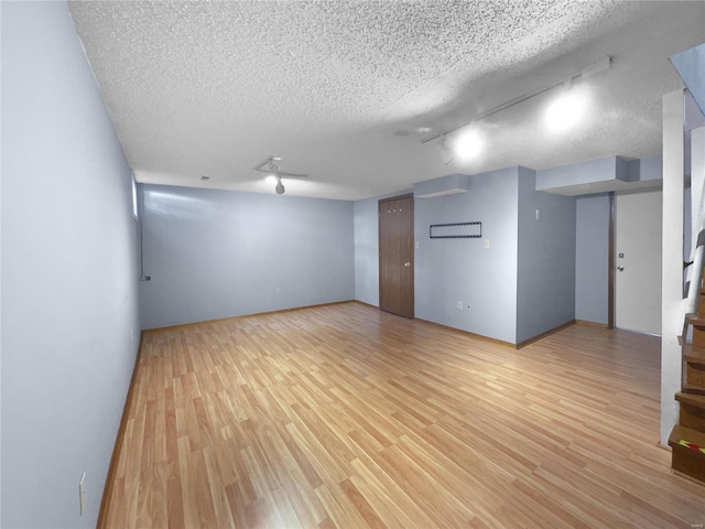 finished basement featuring a textured ceiling, light wood finished floors, and stairs