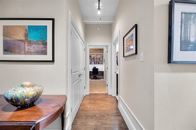 hallway with wood finished floors, a desk, baseboards, and track lighting