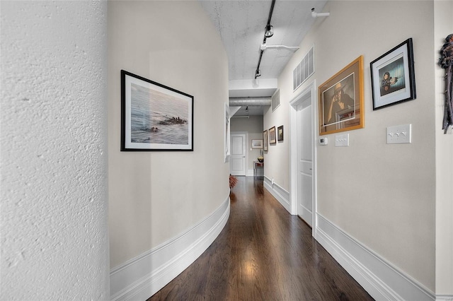 corridor with wood finished floors, rail lighting, and baseboards