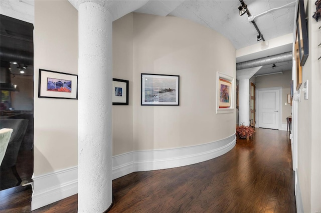 corridor with ornate columns, wood finished floors, rail lighting, and baseboards