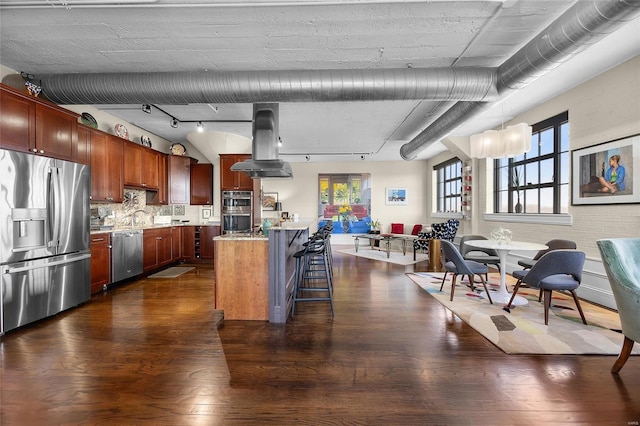 kitchen with appliances with stainless steel finishes, island exhaust hood, a kitchen breakfast bar, and dark wood-style floors