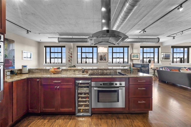 kitchen featuring oven, wine cooler, rail lighting, and dark brown cabinets