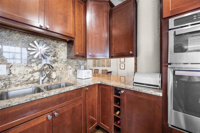 kitchen with a sink, double oven, decorative backsplash, a textured wall, and light stone counters