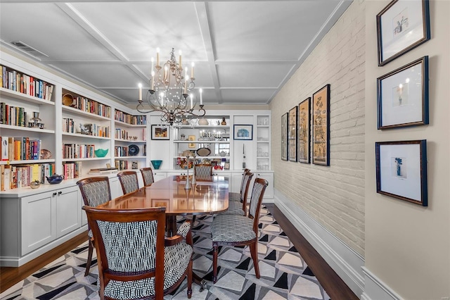 dining space with wood finished floors, brick wall, coffered ceiling, a chandelier, and baseboards