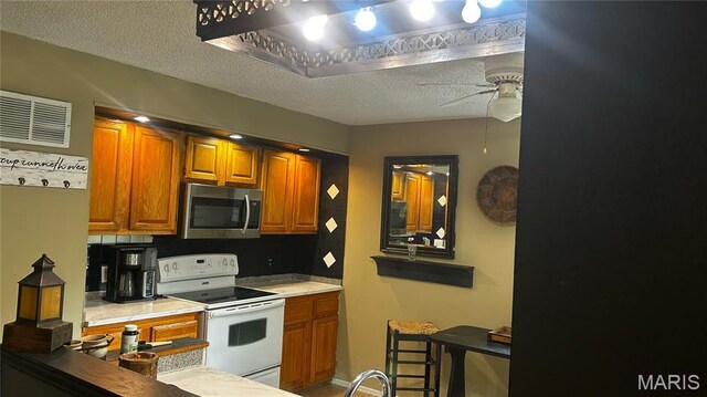 338 Mont Pellier St, Bonne Terre, MO 63628 - kitchen featuring white electric range oven, stainless steel microwave, ceiling fan, brown cabinetry, and a textured ceiling