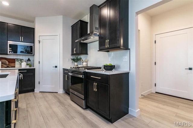 1519 Oglesby Dr, Edwardsville, IL 62025 - kitchen featuring gas stove, wall chimney exhaust hood, dark cabinets, light wood-type flooring, and light countertops