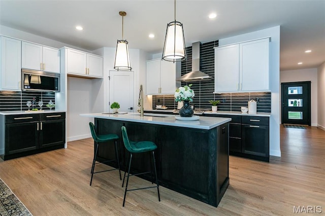 1511 Oglesby Dr, Edwardsville, IL 62025 - kitchen featuring wall chimney range hood, stainless steel microwave, decorative backsplash, light countertops, and white cabinetry