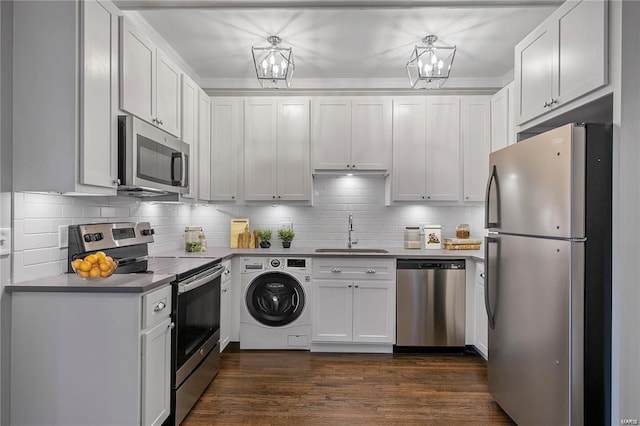 kitchen featuring appliances with stainless steel finishes, washer / dryer, a sink, dark wood-style floors, and backsplash