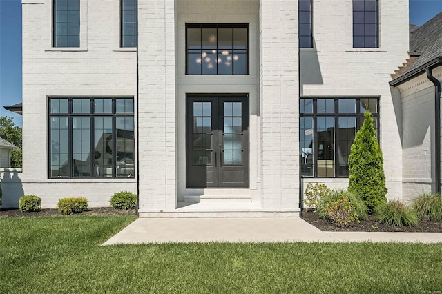 view of exterior entry featuring french doors, brick siding, and a yard
