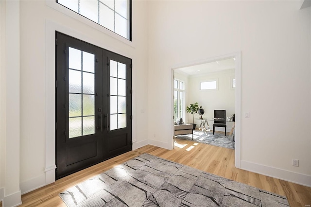 foyer with french doors, light wood-style flooring, baseboards, and a high ceiling