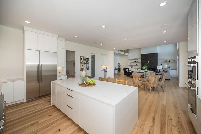 kitchen with modern cabinets, stainless steel built in refrigerator, a kitchen island, white cabinetry, and recessed lighting