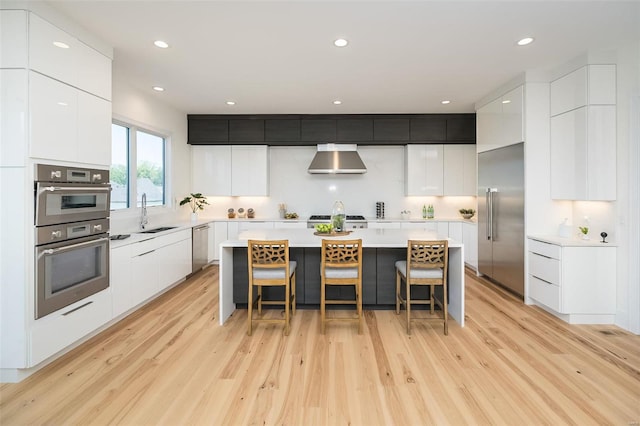 kitchen featuring stainless steel appliances, modern cabinets, wall chimney range hood, a center island, and recessed lighting