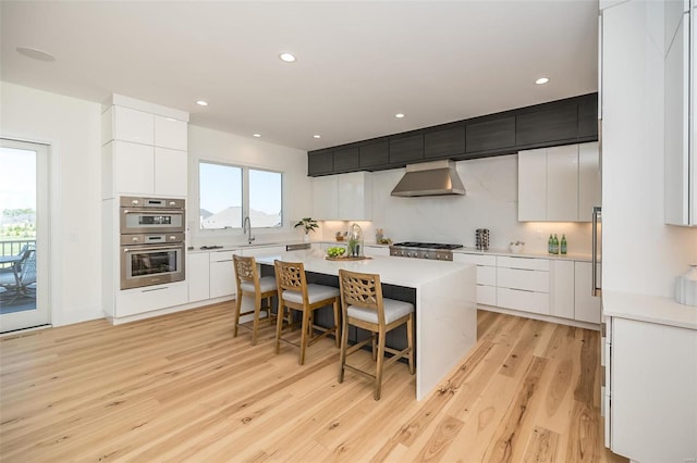 kitchen with wall chimney exhaust hood, modern cabinets, light wood-style flooring, a kitchen island, and recessed lighting